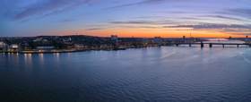 Aerial view of a city waterfront at sunset, with buildings, bridges, and calm water reflecting the evening sky.
