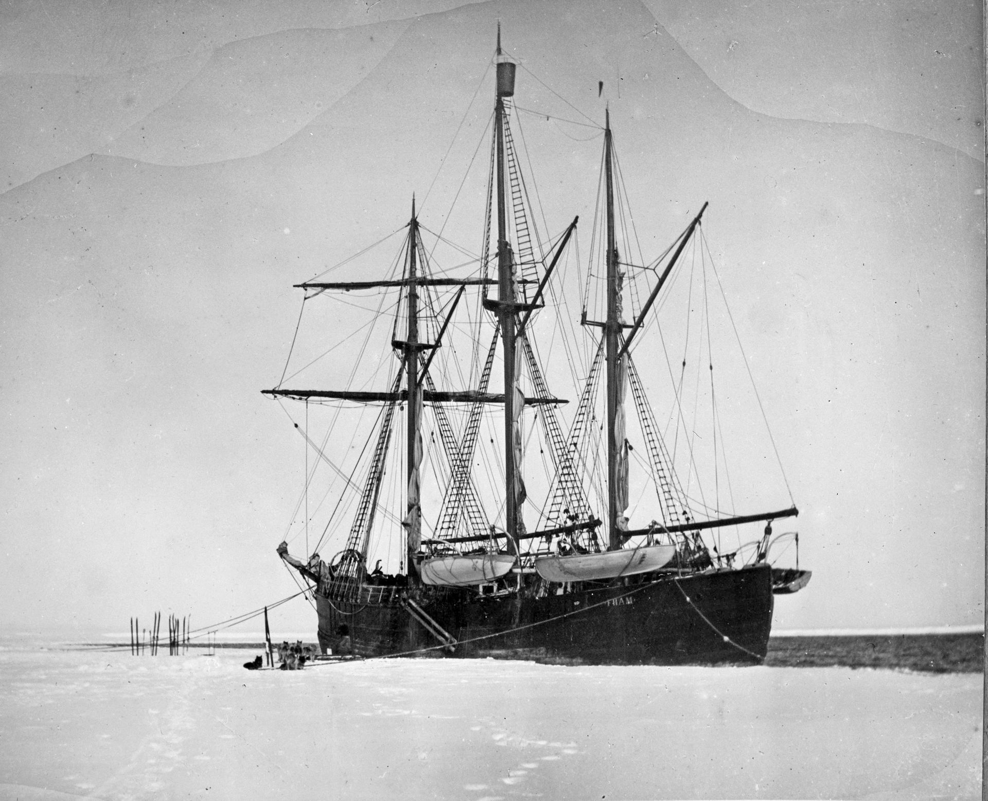 Svart-hvitt bilde av et stort seilskip fastfrosset i isen i et øde vinterlandskap