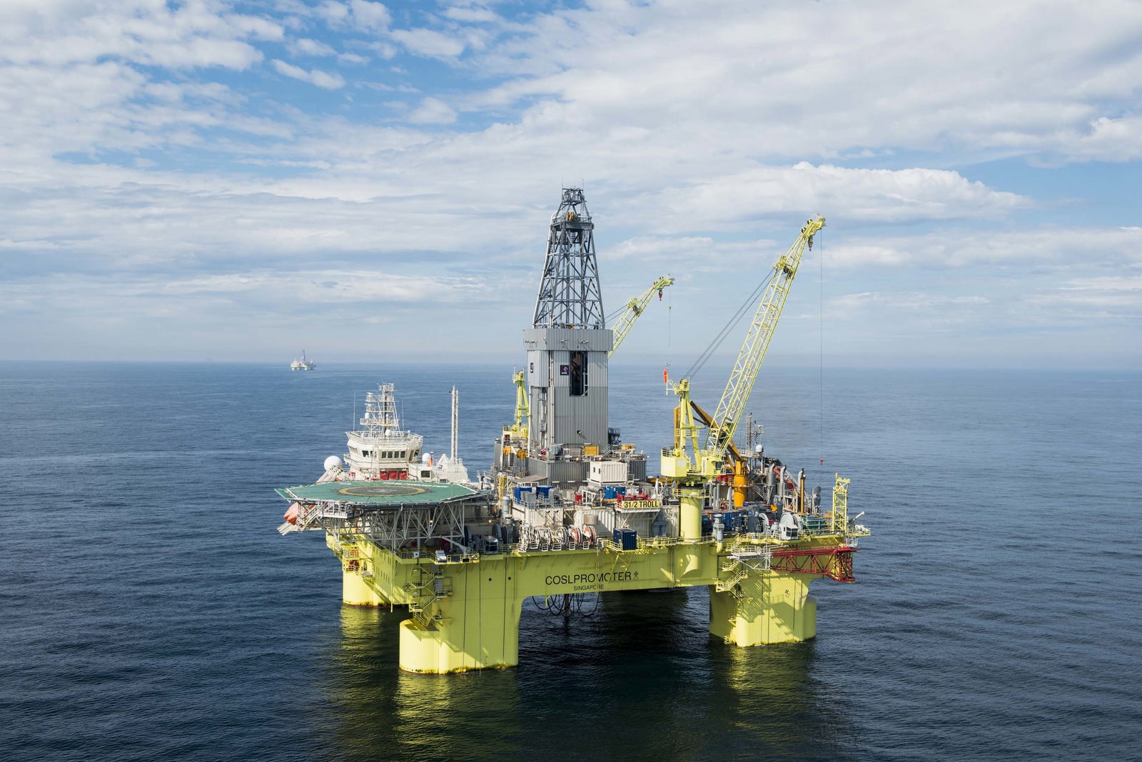 Semi-submersible offshore drilling rig with helipad and drilling derrick operating at sea.