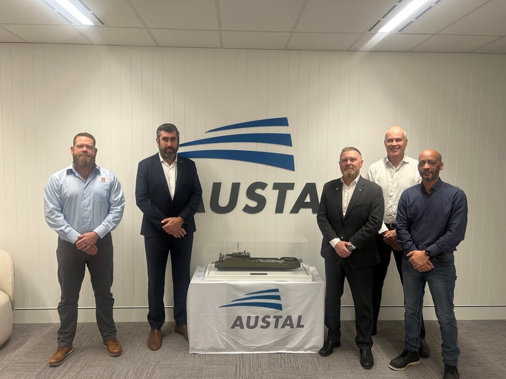 Representatives from Kongsberg Maritime and Austal standing beside a scale model vessel in front of the Austal logo.