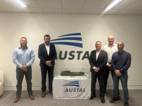 Representatives from Kongsberg Maritime and Austal standing beside a scale model vessel in front of the Austal logo.