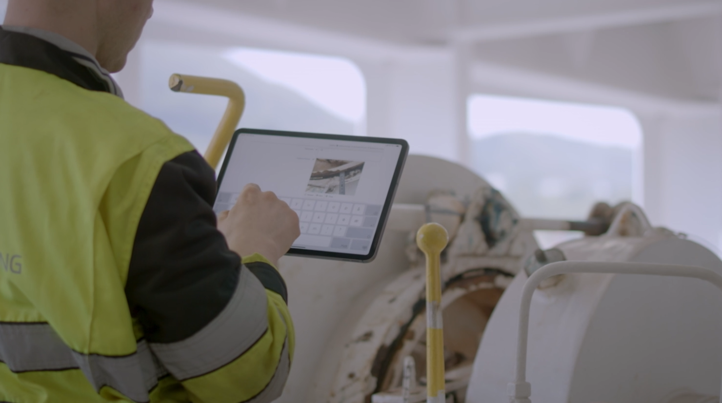 Ship engineer performing check on a winch and filling a digital form on a portable device