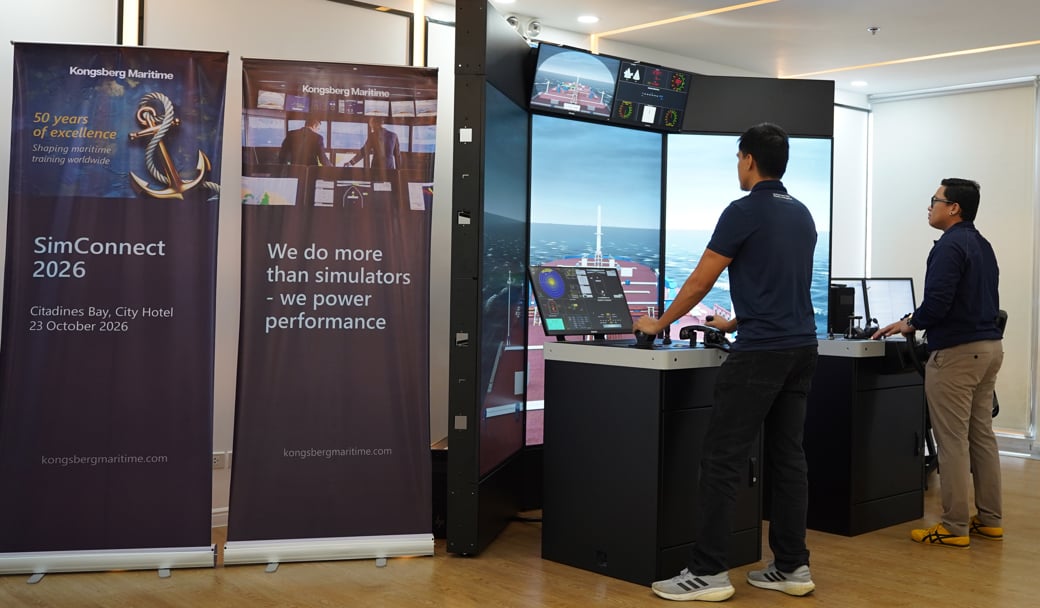 Two people using a maritime simulator with multiple navigation displays at a Kongsberg Maritime simulation setup.