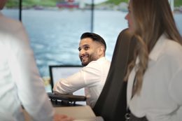 Colleagues seated at workstations on a vessel bridge, discussing work with large windows overlooking the sea.