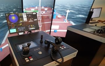 Maritime simulator control station with navigation displays and a simulated vessel at sea.