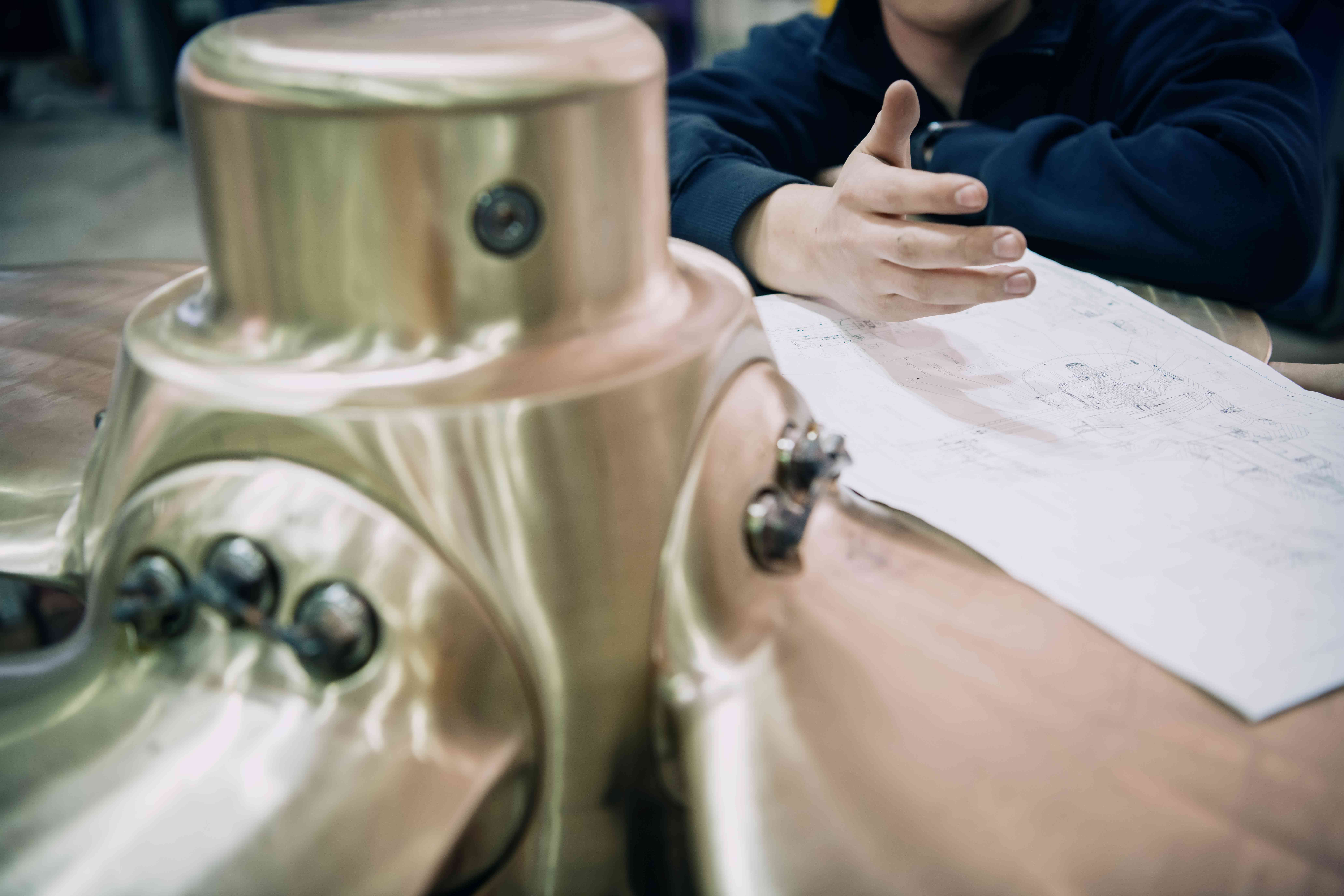 Close-up of a thruster controllable pitch propeller hub with a person’s hand resting on technical drawings on the blades