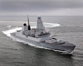 A grey naval vessel making a sharp turn at sea, leaving a circular wake pattern behind under an overcast sky.