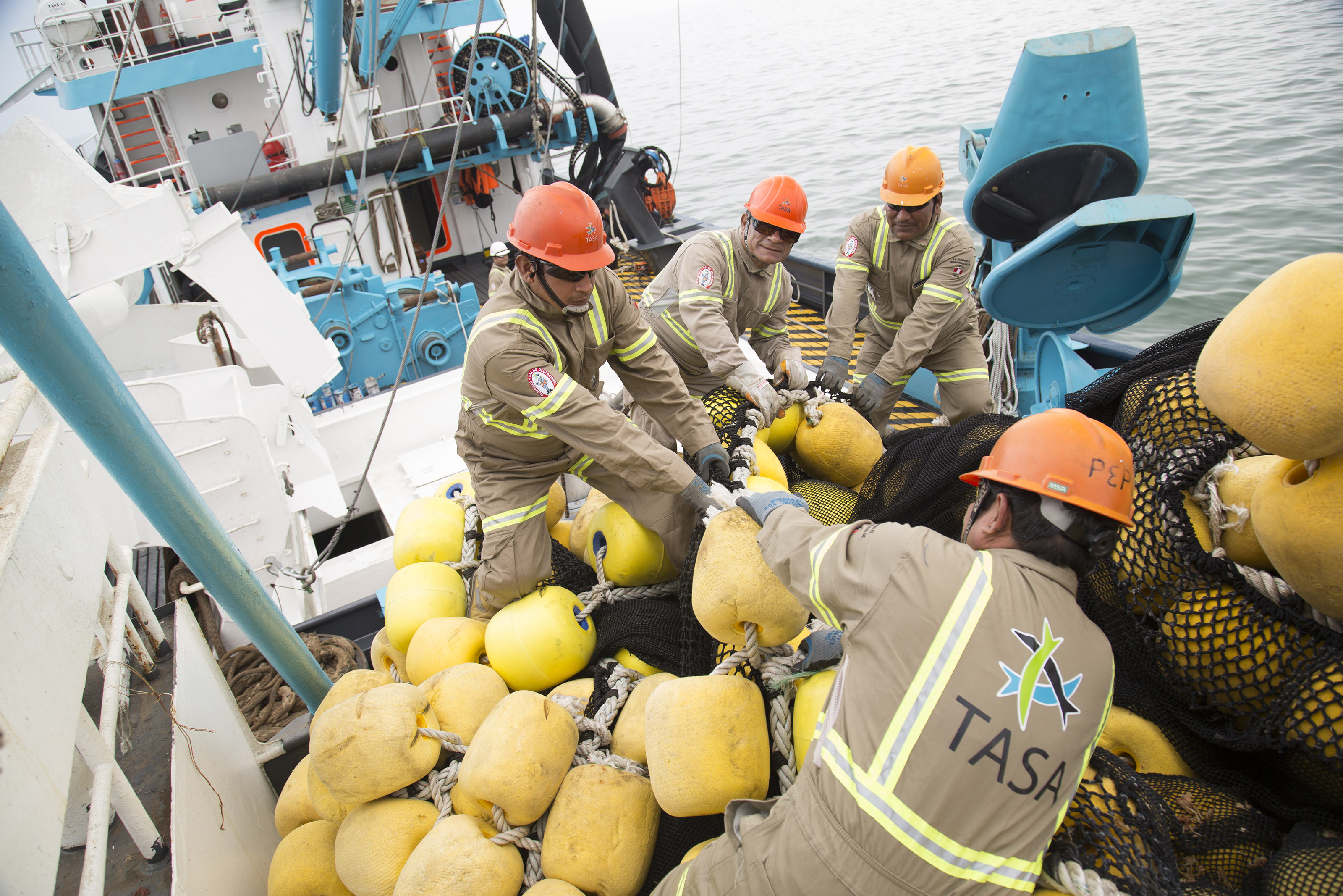 Four fishermen onboard the fishing vessel pulling up the yellow floaters of the fishing net. 