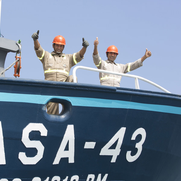 Two happy fishermen onboard the fishing boat, both smiling and showing two thumbs up.