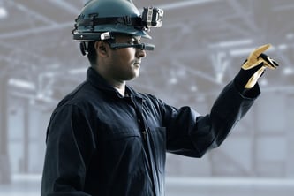 A vessel technician wearing protective gear, a headlight, and a mixed reality headset and pointing to equipment onboard to enable remote inspection and troubleshooting by a service expert