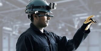 A vessel technician wearing protective gear, a headlight, and a mixed reality headset and pointing to equipment onboard to enable remote inspection and troubleshooting by a service expert