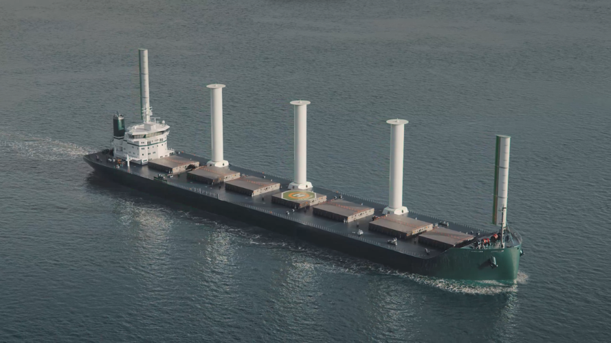 Moderne lasteskip med fire høye, sylindriske seil som seiler på åpent hav.