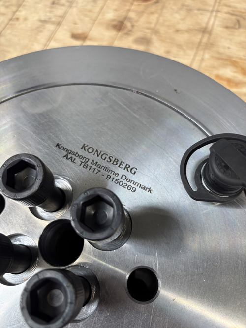 Close‑up of a circular metal industrial component with a handle, placed on a work surface in a workshop environment.