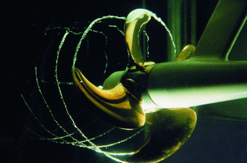 A marine propeller undergoing hydrodynamic testing in water, with visible cavitation trails forming behind the blades.