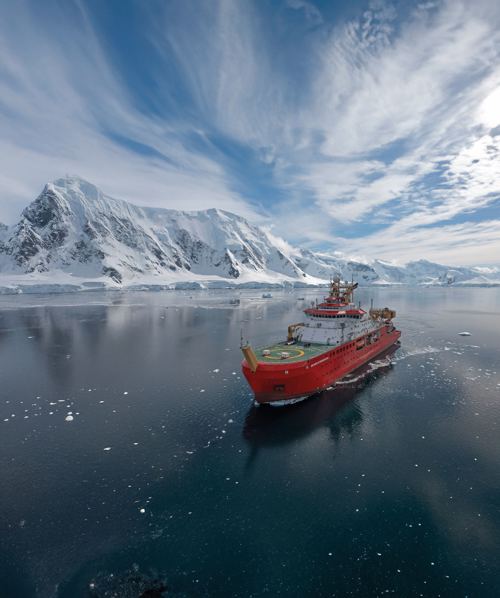 Red vessel navigating through icy waters in a polar region, surrounded by floating ice and snow-covered mountains.