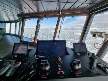 A ship's bridge with a computer display looking over an icy sea