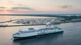 Scandlines's hybrid vessel Schleswig Holstein, sailing in calm waters alongside a small pleasure boat harbour at sunrise