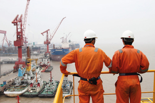 Two Kongsberg Maritime field service engineers at a port in Shanghai with multiple vessels moored in the background