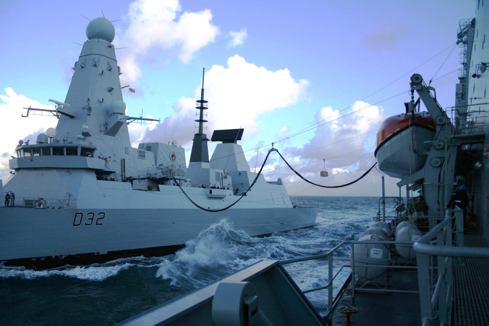 Two naval vessels side by side at sea using the replenishment at sea technology.