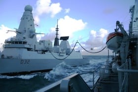 Two naval vessels side by side at sea using the replenishment at sea technology.