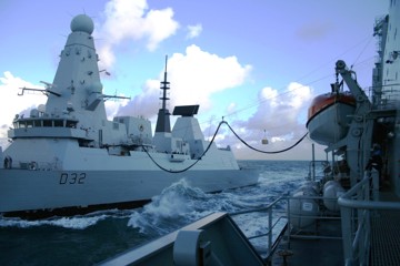 Two naval vessels side by side at sea using the replenishment at sea technology.