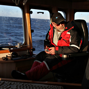 A fishing boat captain sitting on the bridge of the boat, with the open sea in the background