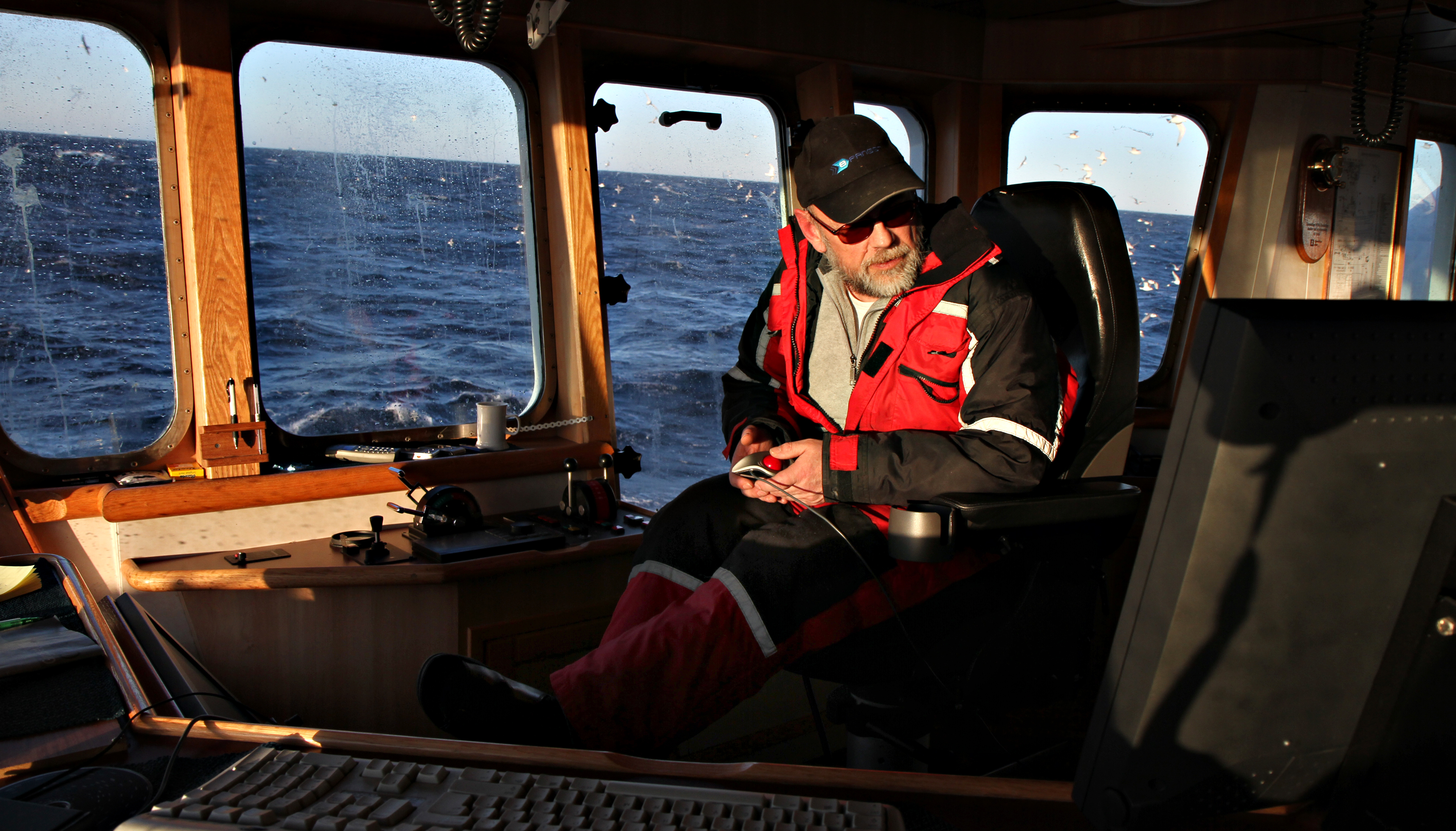A fishing boat captain sitting on the bridge of the boat, with the open sea in the background