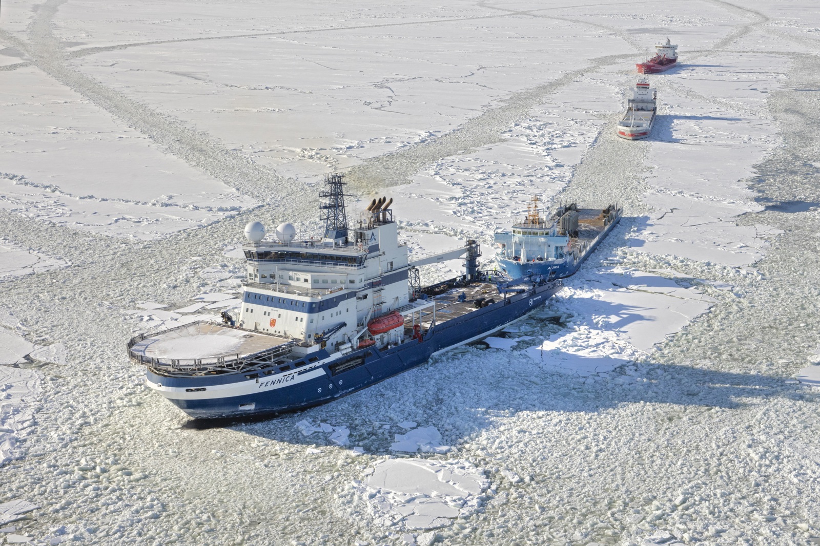 Aerial view of an icebreaker creating a wide channel through dense sea ice, with another vessel following behind.
