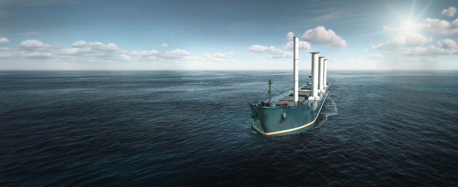 Vessel sailing across a calm open ocean fitted with four tall wind-assist rotor sails, viewed from above under a bright sky, illustrating sustainable maritime propulsion and fuel-efficiency technologies.